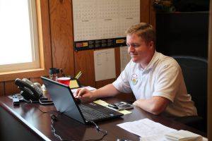 Young man working at desk with laptop and office supplies in a wooden office.