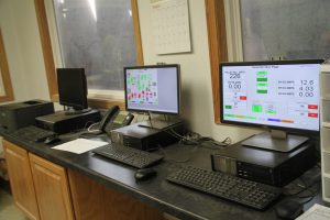 Computer workstation with monitors, keyboard, and office equipment in a control room.