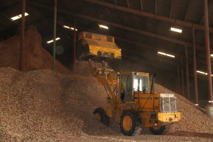 Heavy machinery moving wood chips in a large industrial warehouse.
