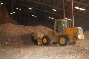 Heavy-duty John Deere wheel loader moving wood chips in a warehouse.