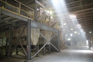 Industrial cob processing equipment in a factory setting with sunlight streaming in.