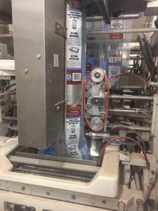 Automated packaging machine sealing plastic bags with product inside.