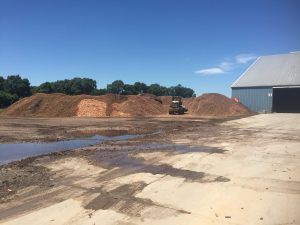 Large piles of organic cob material at a farm with a tractor and barn in the background.