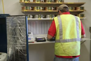 Worker in safety vest at checkout counter with jars on shelves in background.