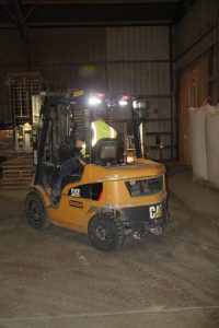 Forklift operator in warehouse with worker and storage racks.