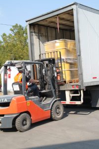 Forklift loading large yellow containers into a delivery truck at Best Cob.