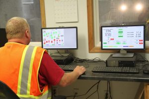 Worker monitoring control panels on dual computer screens in a control room.