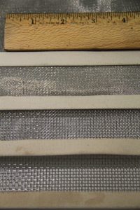Various types of window screens and mesh materials displayed with a ruler for size comparison.