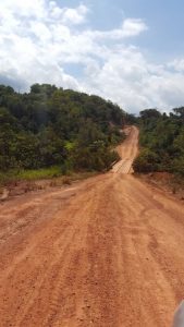 Dirt road winding through green hilly landscape under cloudy sky.