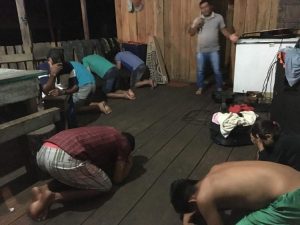 Group of people praying together in a wooden room, some kneeling and some standing.