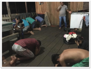 Group of people praying together in a rustic indoor setting with wooden walls.