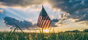 American flag waving in a field at sunset with dramatic clouds in the sky.