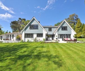 Modern white house with large lawn and blue sky in the background.