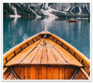 View from a wooden boat on a serene mountain lake with snow-capped peaks.