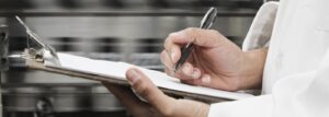 Person taking notes on a clipboard in a professional kitchen setting.
