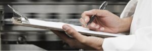 Chef writing on a clipboard in a professional kitchen setting.