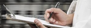 Person writing on a clipboard in a professional kitchen setting.
