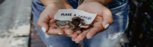 Hands holding coins and a note saying 'Make a Change' for charity or donation.
