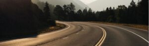 Scenic mountain road with curves surrounded by trees and foggy mountains in the background.