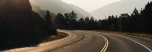 Scenic mountain road with curves and forested surroundings at sunset.