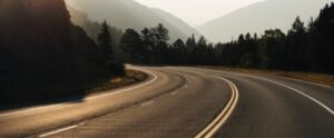 Scenic mountain road with curves and forested surroundings at sunset.