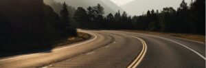 Winding mountain road with trees and mountains in the background.