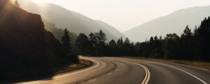 Scenic mountain road with trees and misty mountains in the background.