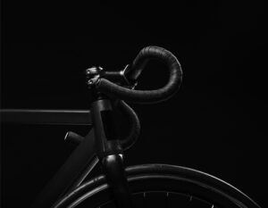 Close-up of a black bicycle handlebar and front wheel on a dark background.