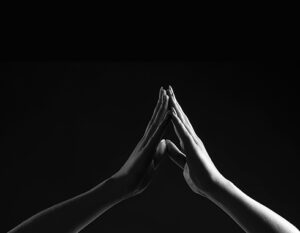 Two hands touching in a prayer position against a black background.
