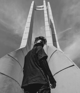 Person standing under a modern architectural structure with a cloudy sky background.